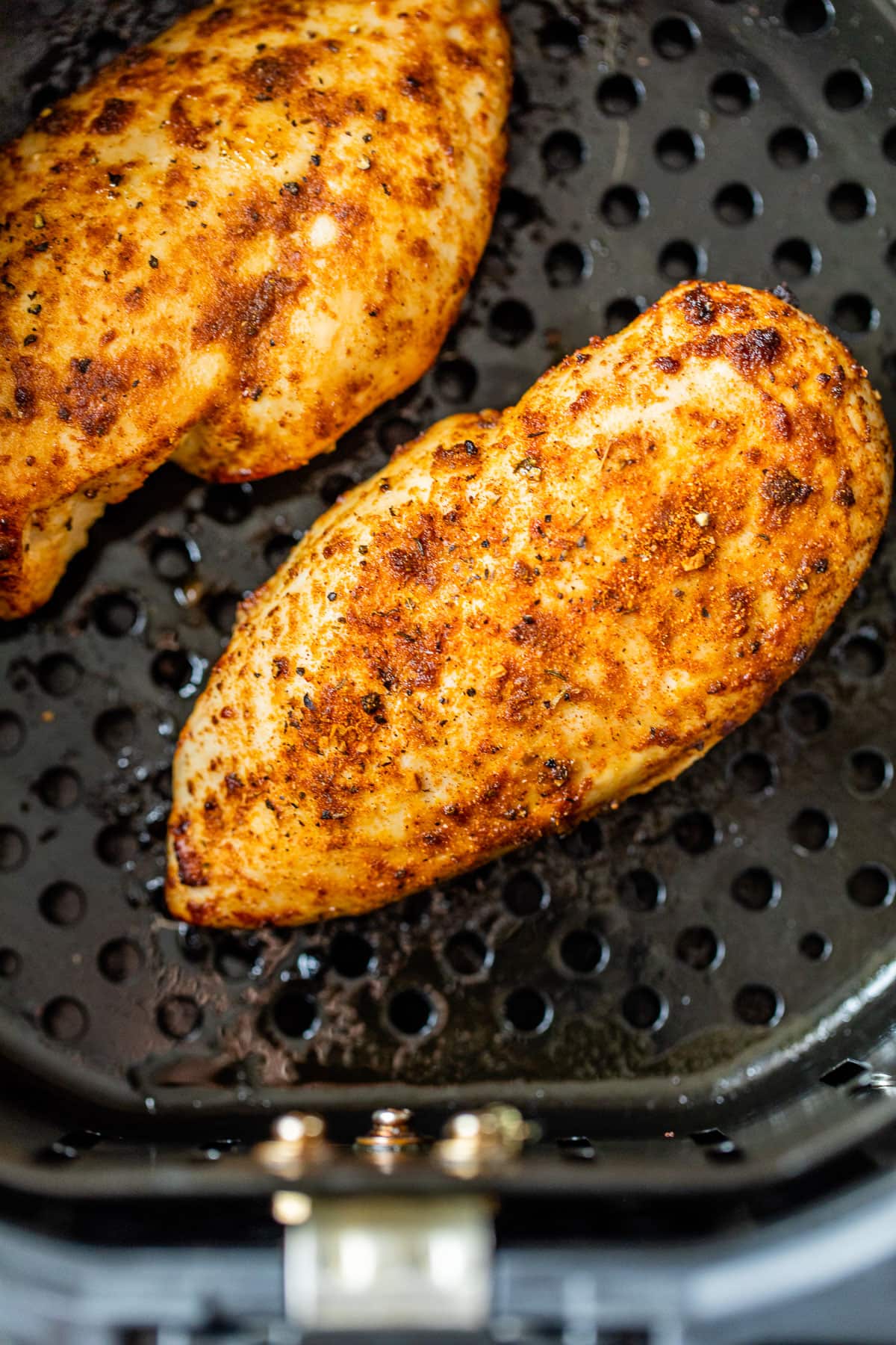 Two air fryer chicken breasts with seasoning