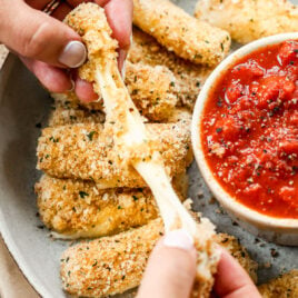 baked mozzarella sticks with marinara sauce being pulled apart with cheese pull