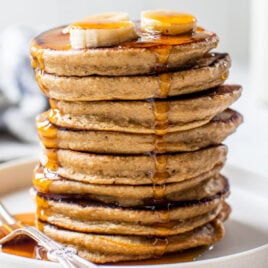 a stack of banana oatmeal pancakes no flour on a plate with banana and maple syrup