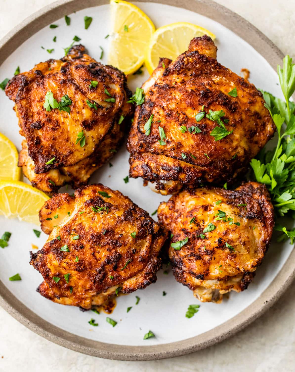 Four air fryer chicken thighs on a plate with lemon slices