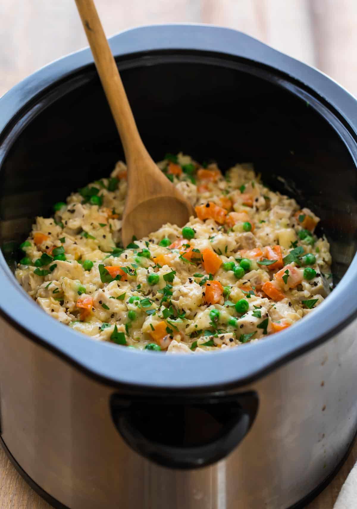 crock pot chicken and rice with vegetables being stirred with a wooden spoon