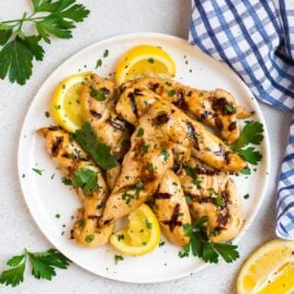 Delicious grilled chicken tenders on a white plate with lemon slices