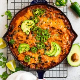 Cheesy skillet chicken enchiladas, served in a skillet and topped with avocado