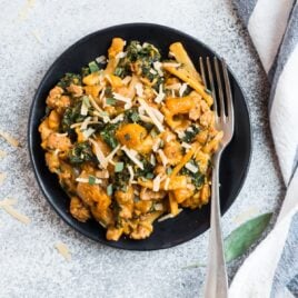 A plate of creamy butternut squash pasta with chicken sausage, kale, and Parmesan topped with sage