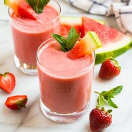 Two glasses of a creamy watermelon smoothie with strawberry and mint