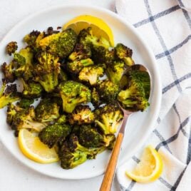 A white plate with roasted frozen broccoli and lemon slices