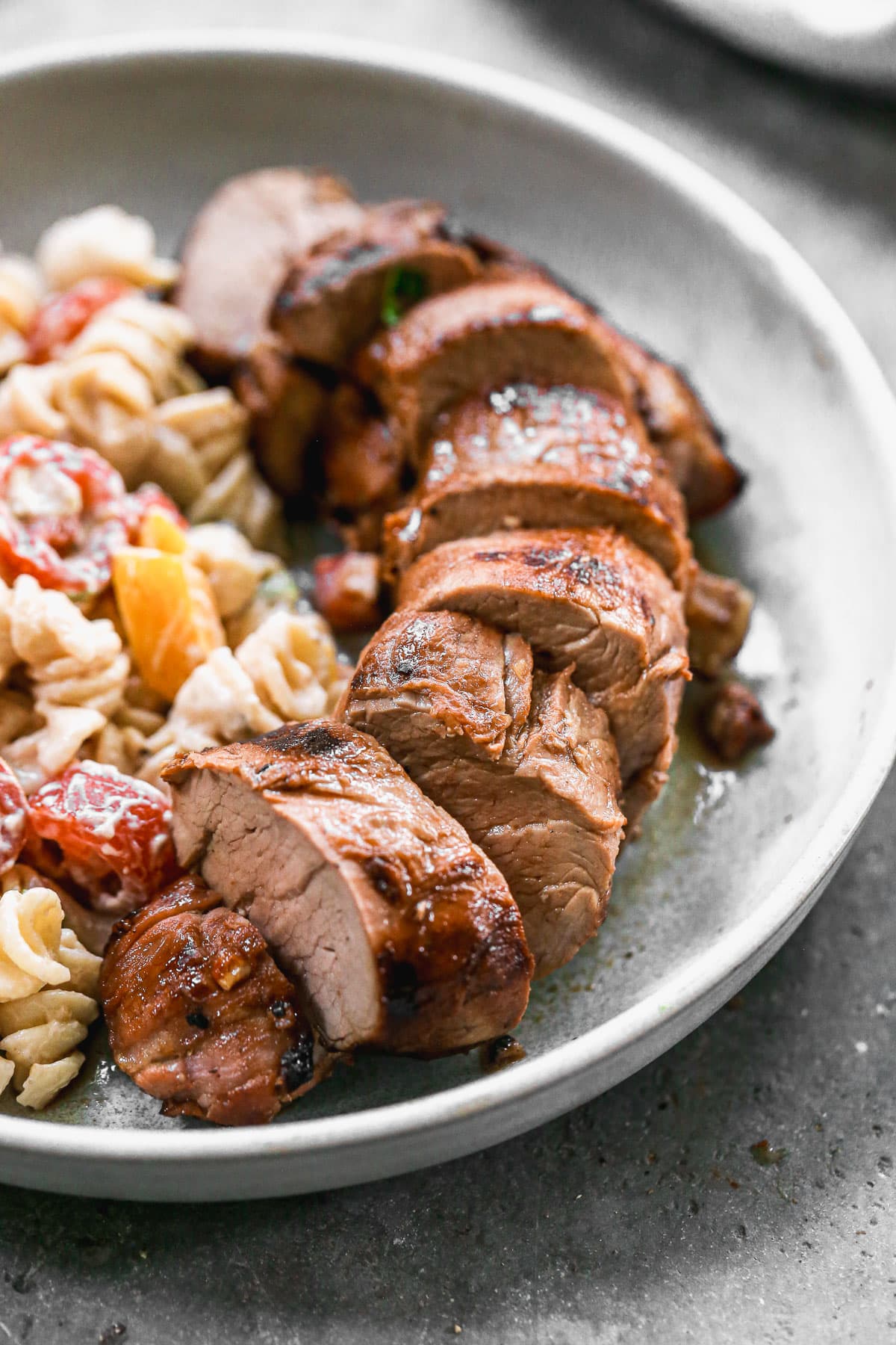 juicy grilled pork tenderloin slices on a plate with pasta salad
