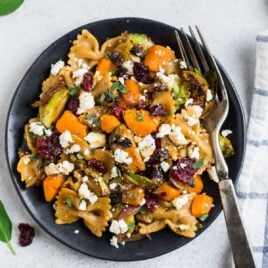 A plate with healthy sweet potato pasta with Brussel sprouts and cranberries on a black plate.