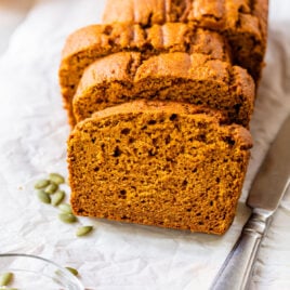 slices of low fat pumpkin bread on a piece of white parchment baking paper with a knife and pumpkin seeds