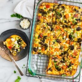 A pan with a vegetarian breakfast casserole sliced for a crowd with a slice of the casserole on a plate