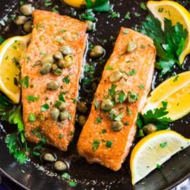 A skillet with two fillets of salmon meuniere with lemon, butter, and parsley