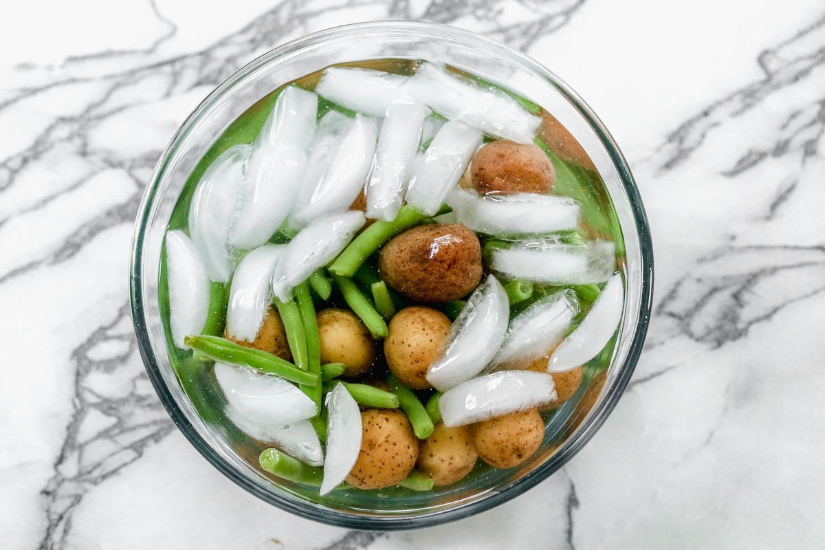 A bowl of ice water with potatoes and green beans