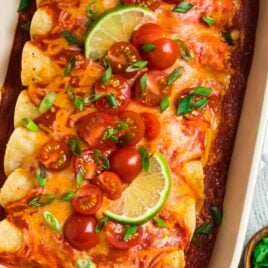 A blue casserole dish with creamy Instant Pot Chicken Enchiladas, topped with red enchilada sauce and cheese