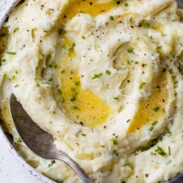 serving bowl filled with Instant Pot mashed potatoes, garnished with fresh herbs and melted butter