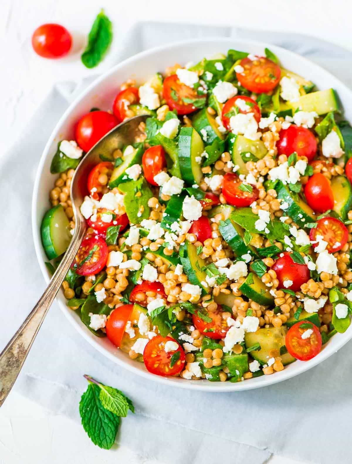Mediterranean Israeli Couscous Salad with Feta and Mint in a white salad bowl, with a spoon for serving