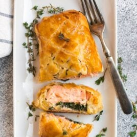 A white plate with salmon wellington, a dish of salmon on spinach, wrapped in puff pastry and baked