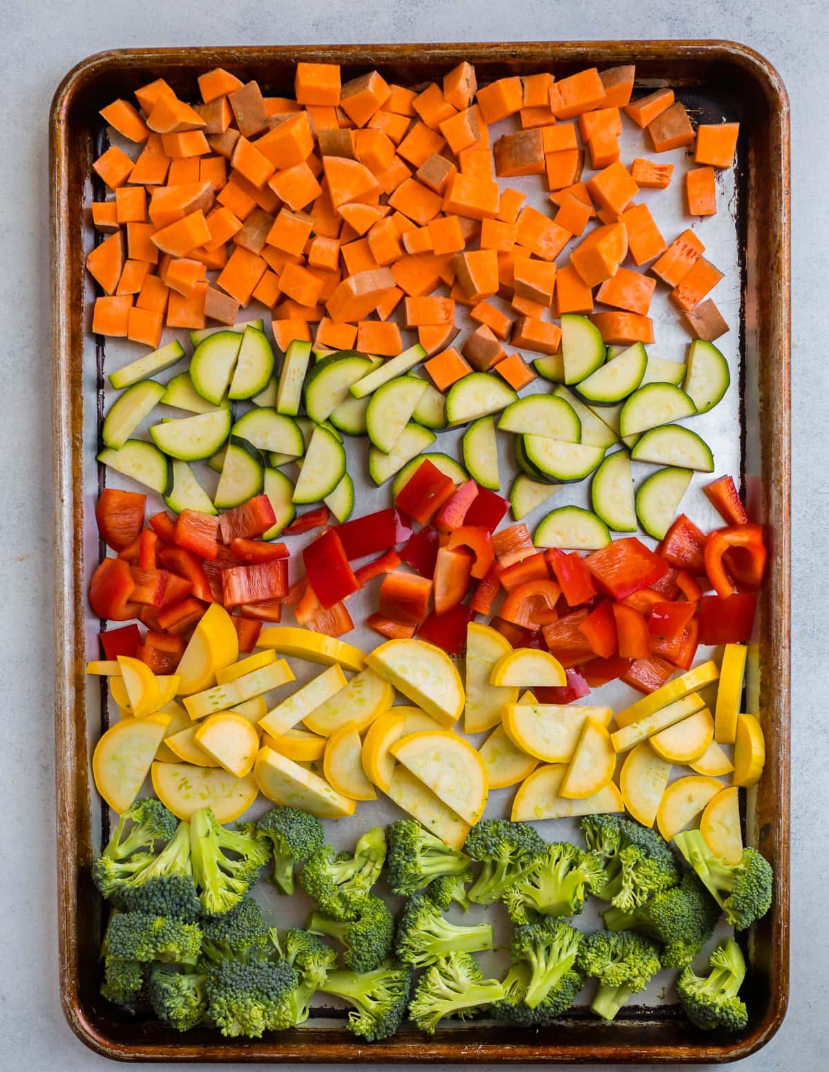 Chopped sweet potatoes, zucchini, peppers, squash, and broccoli on a baking sheet
