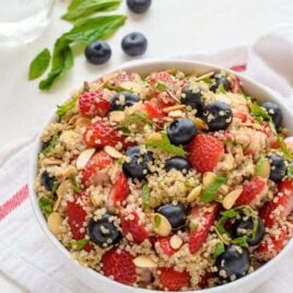 Red white and blue quinoa fruit salad in a white bowl