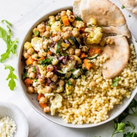 Roasted vegtable salad in a bowl with quinoa and pita