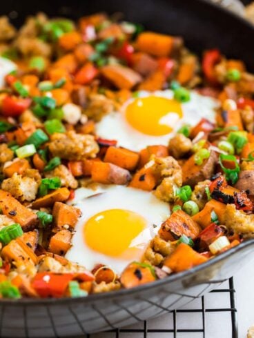 a close up of an egg cooked on top of sweet potato hash with sausage and green onion