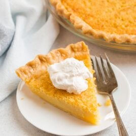 A slice of buttermilk pie on a white plate with whipped cream