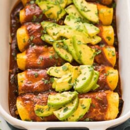 Easy Vegan Enchiladas with tofu, spinach, and black bean filling, topped with a rich and flavorful red enchilada sauce and avocado. This recipe is THE BEST! Healthy, packed with protein, entirely plant based, dairy free (you won’t miss the cheese!), and gluten free. Casserole is freezer friendly and can be made in advance.