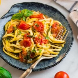 Zucchini pasta on a blue plate with tomatoes